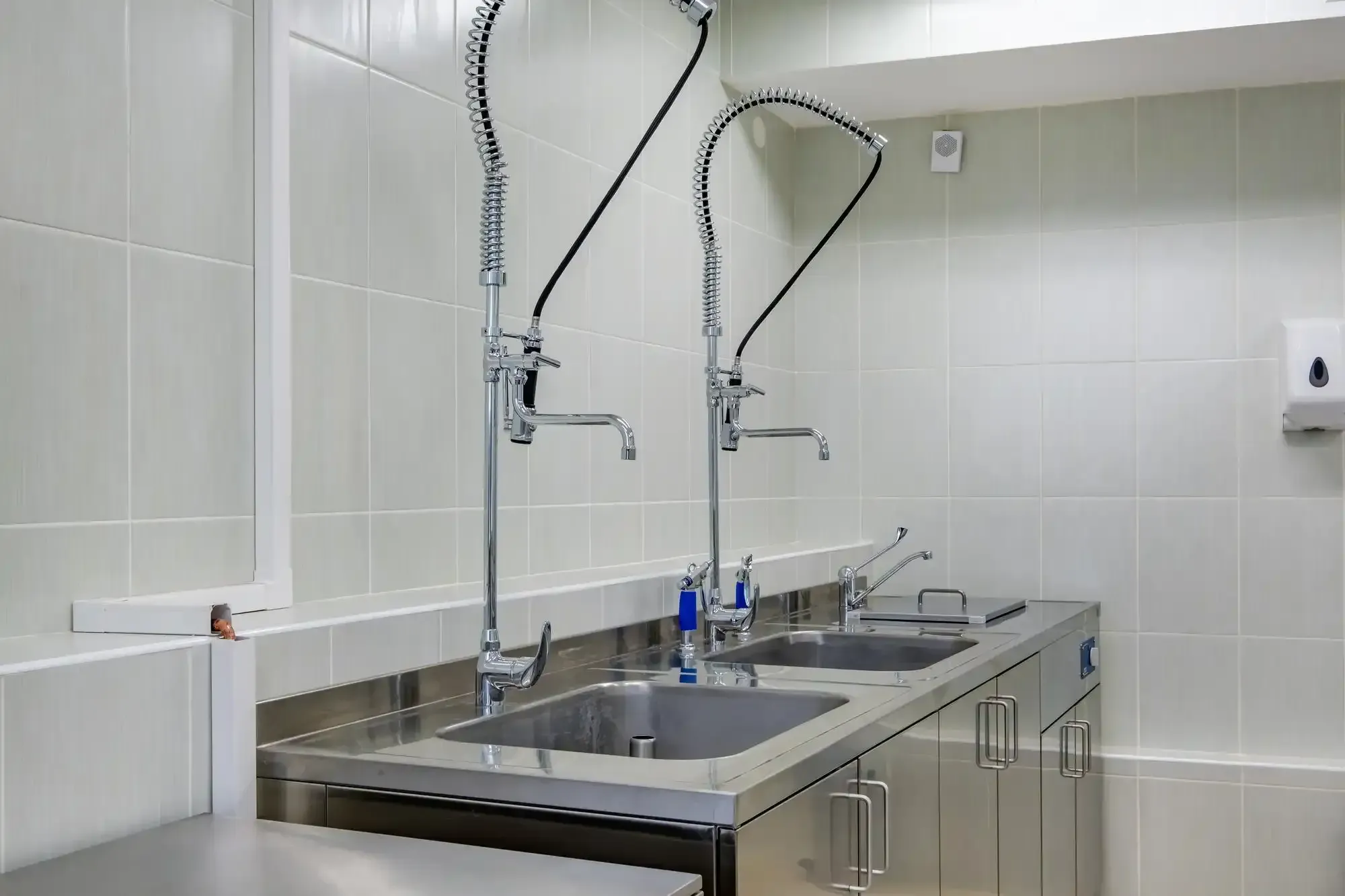Stainless steel sinks and faucets in a clean, tiled room.