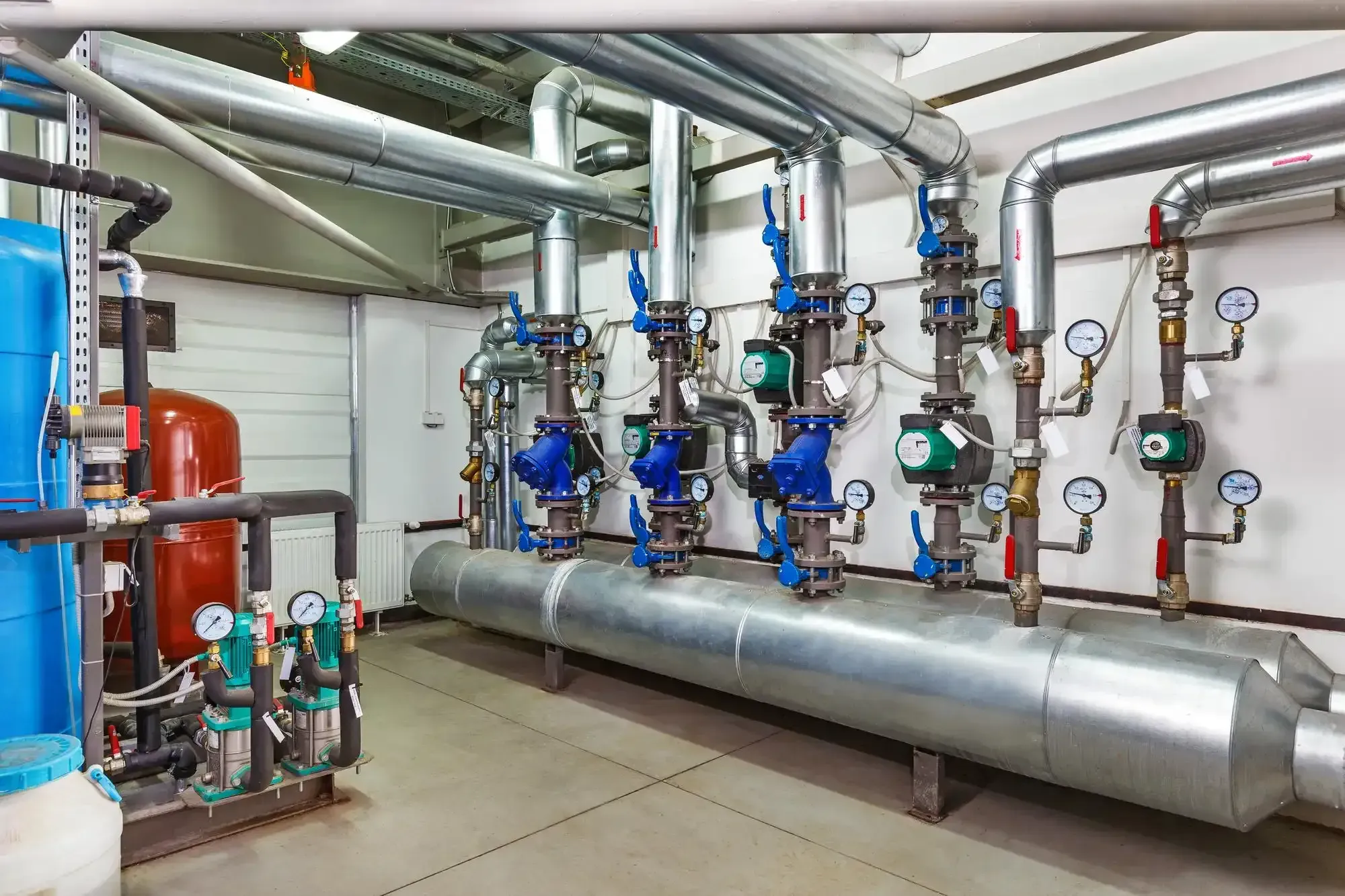 Pipes and valves in a utility room; silver and blue, with gauges and insulation, possibly for heating or cooling.