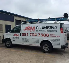 White J&M Plumbing van parked in front of a building. Van has the company logo and phone number.