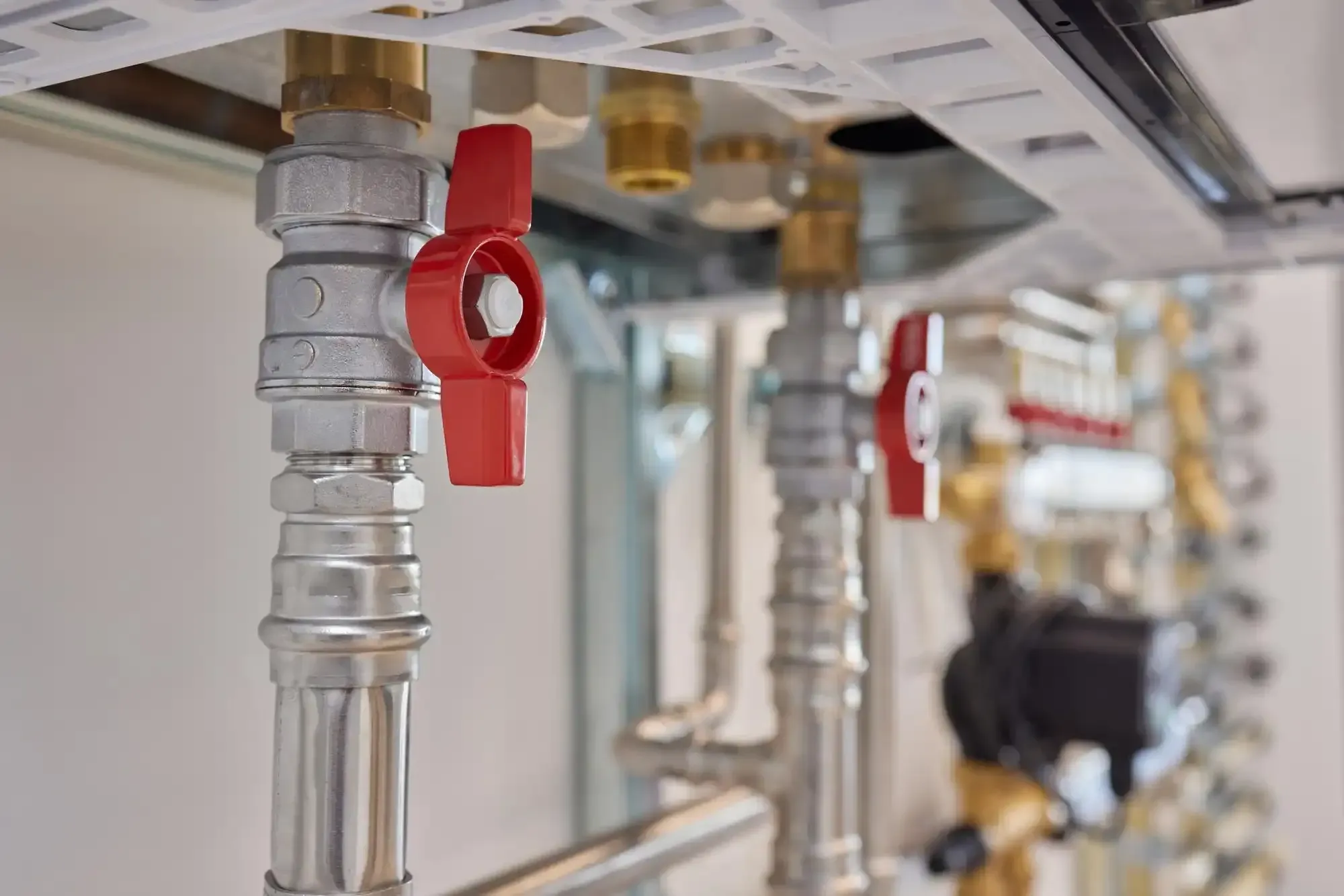 Close-up of plumbing pipes with red valve handles, a metallic infrastructure with a blurred background.