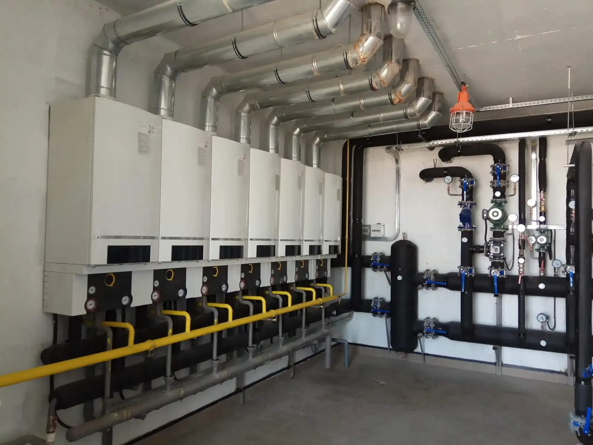 Industrial boiler room with multiple white boilers and pipework.