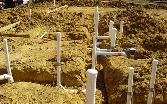 White PVC drainage pipes stubbed up through a sand pad on a commercial construction site.