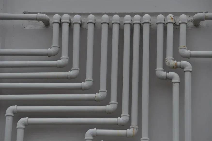 White pipes arranged on a gray wall, forming a network of plumbing.